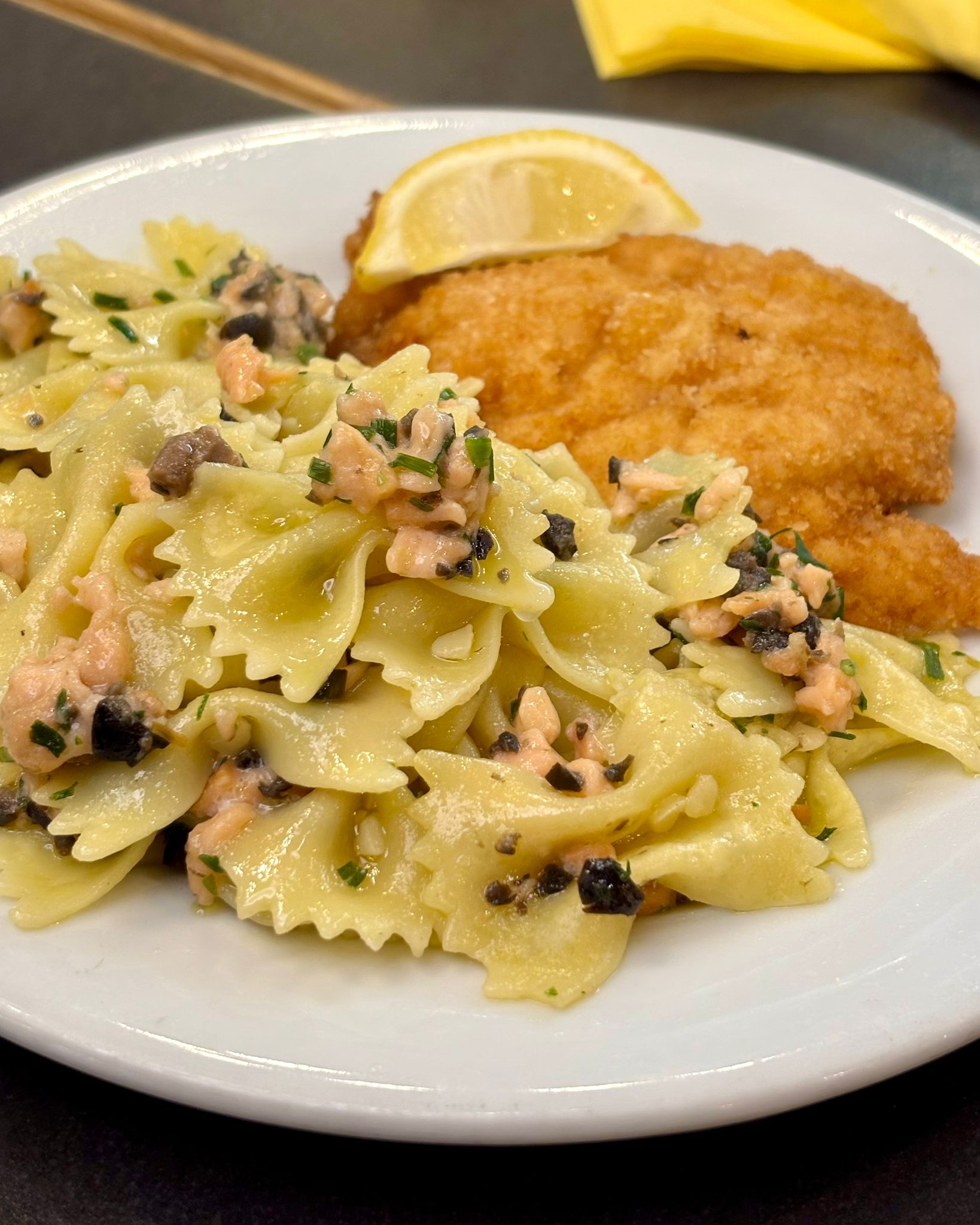 Photo montrant une escalope de poulet à la Milanaise accompagnée de farfales au saumon 		fumé, olives, ciboulette servie au restaurant Caffè Corto à Paris 8 Madeleine 11 rue Tronchet